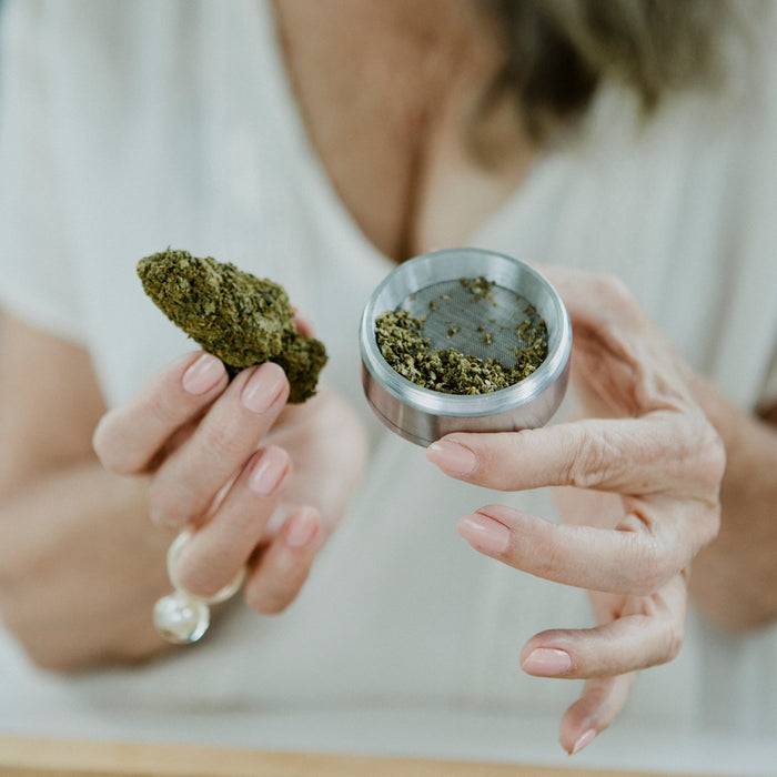 Person holding a cannabis bud and grinder against a neutral background